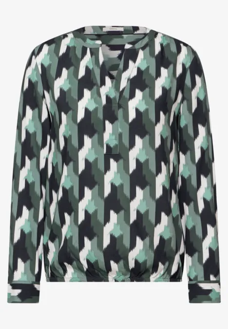 Bluse mit grün-schwarzem geometrischem Muster und V-Ausschnitt.